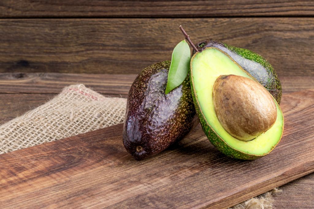 Fresh avocado on cutting board over wooden background