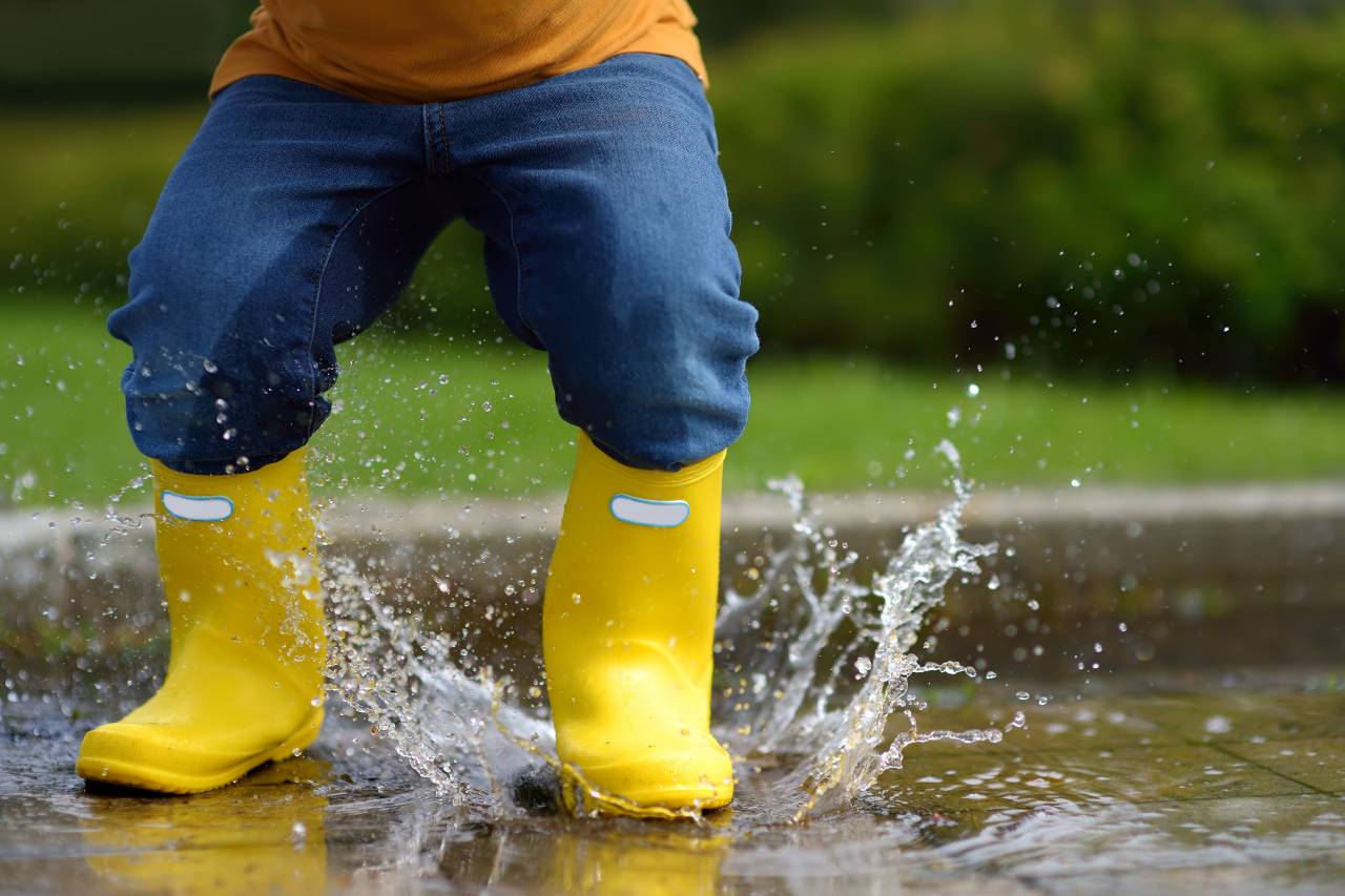 Child splashing in a puddle in yellow boots in a child care facility in Contra Costa County.