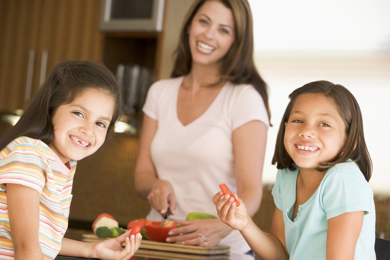 A mother and two kids eating vegetables representing eating healthy with California food stamps.