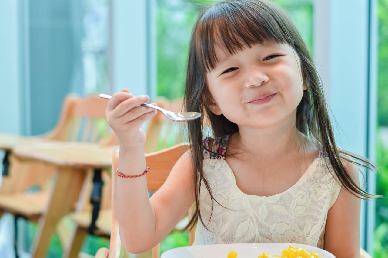 Smiling toddler girl eating corn representing Pandemic EBT Food Benefit for Children in Contra Costa County.
