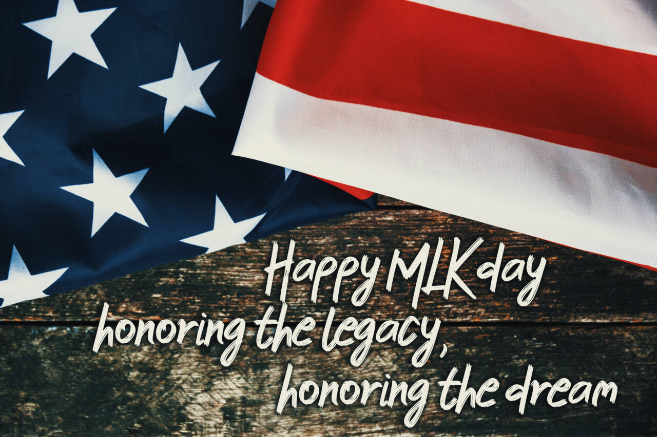 An American flag draped over a dark wooden surface with the text "Happy MLK day honoring the legacy, honoring the dream" written across the wood.