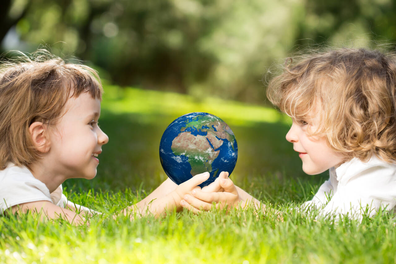 Two children lying in the grass holding a small globe, representing the future-focused mission of child care advocacy.