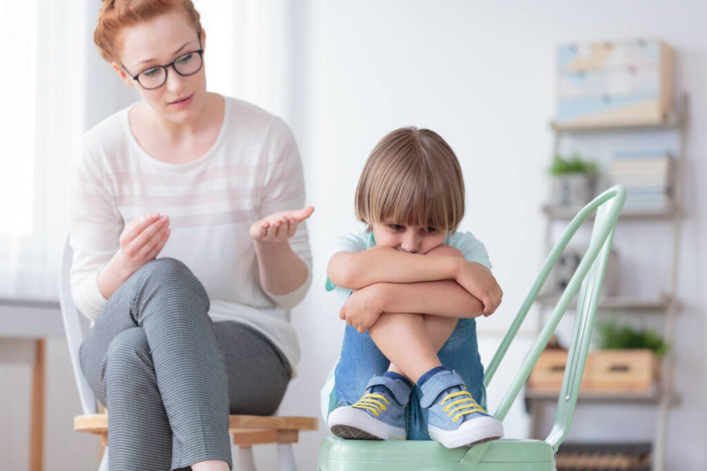 Worried autistic Boy Sitting With Crossed Legs On a Chair while a child care provider is talking to him.