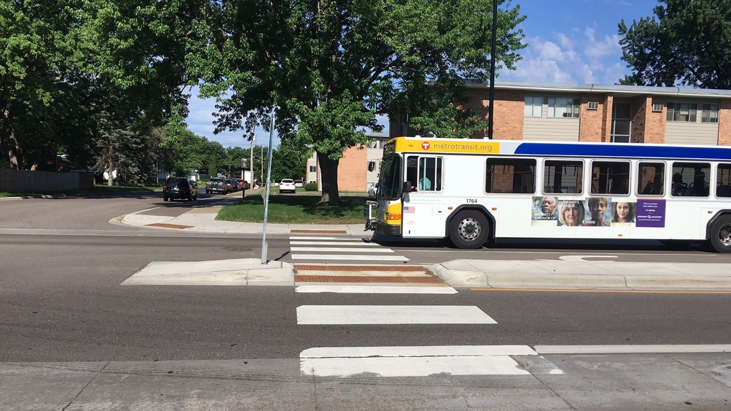 A crosswalk with a median in the middle of it and a bus on the opposite side of the street