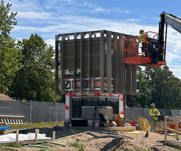 A small mockup of the larger structure includes steel framing, glass, concrete, and wood elements for testing purposes. The mockup is a small square structure with all building elements included.