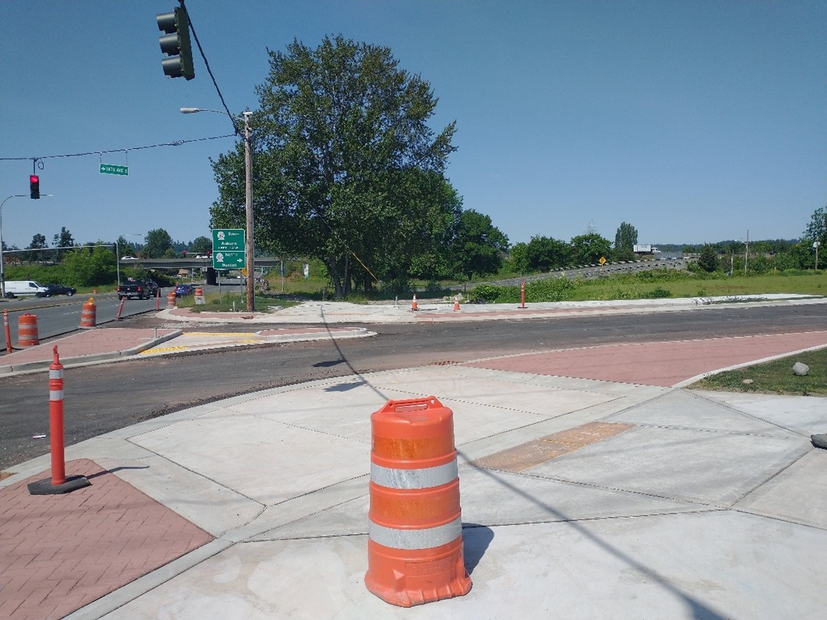 An image showing a a driveway modification to minimize exposure to pedestrians crossing the street. The curb ramp each has a red mountable truck apron. The crosswalk walk from both curb ramps each lead to a new pedestrian refuge island. There are temporary orange traffic barrels around the truck apron and island as the picture was taken during construction.