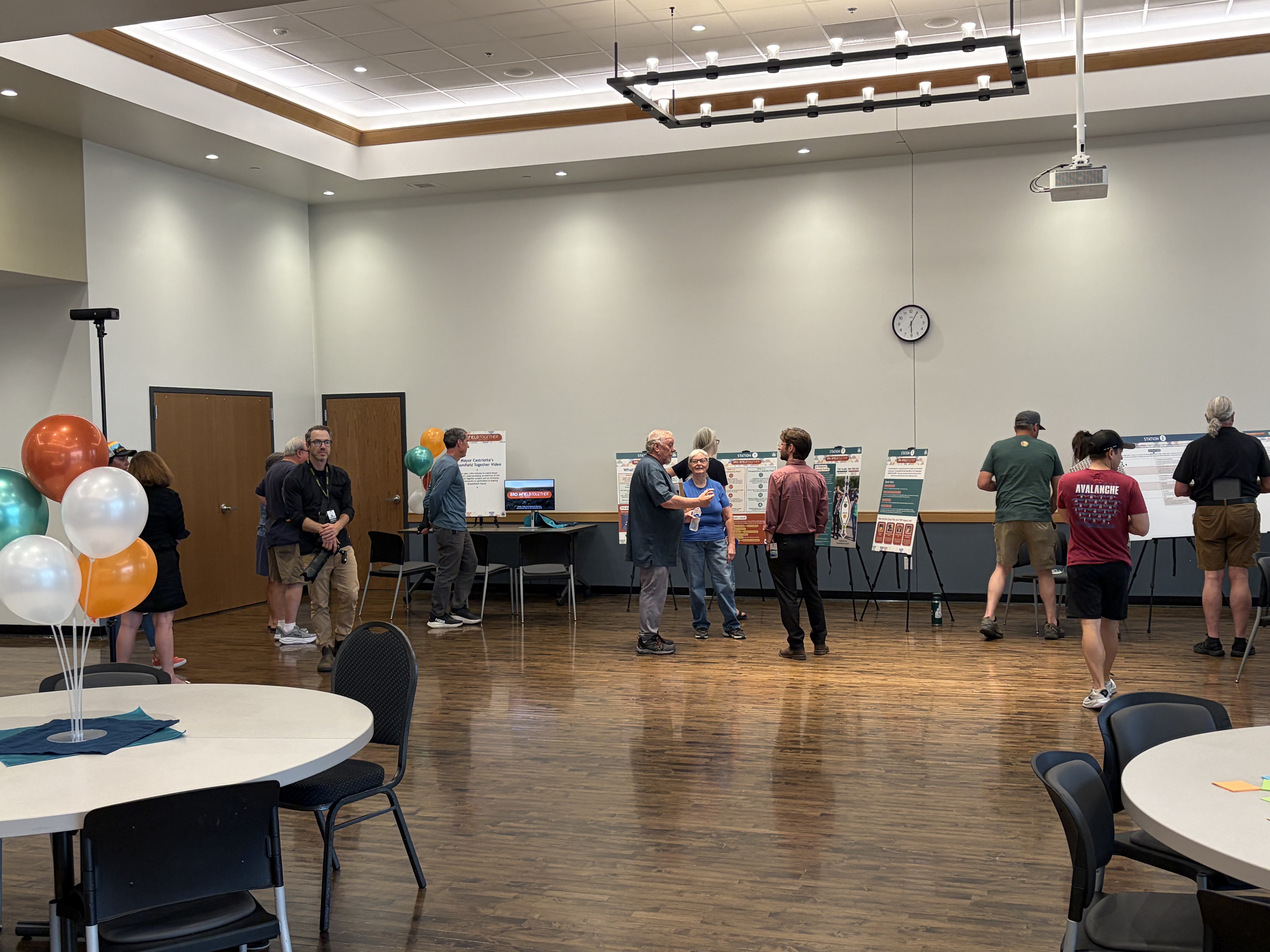 A community engagement open house where participants interact with informal posters and easels. People stand in small groups discussion and providing feedback on local planning initiatives.