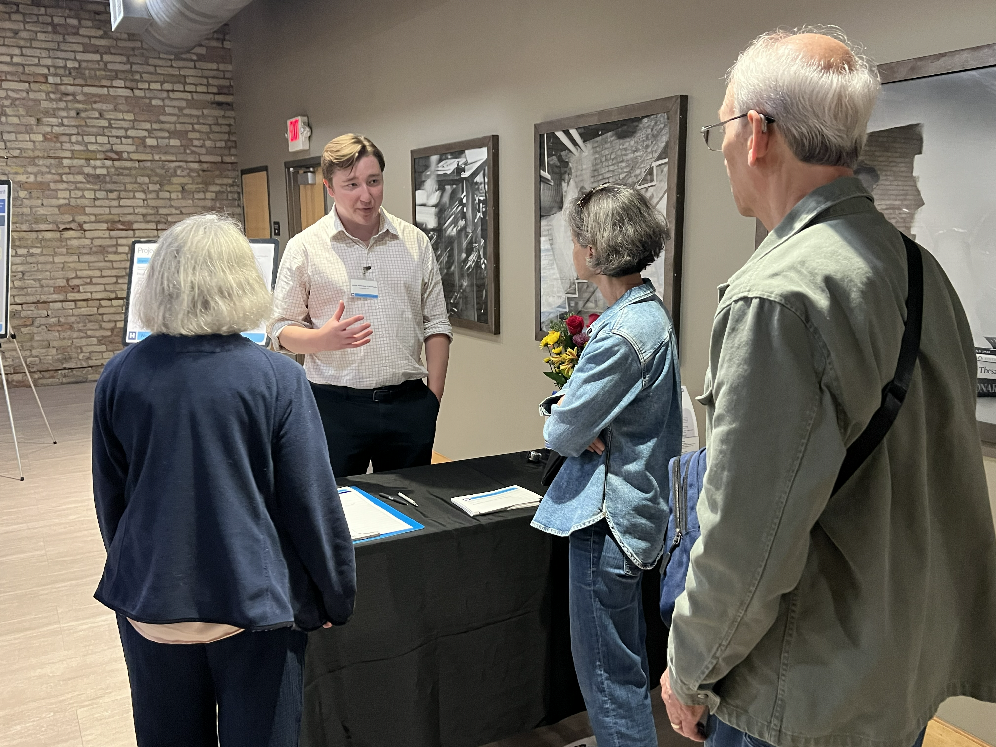 A project staff member is standing in front of a table with black cloth, and is talking to a group of people.