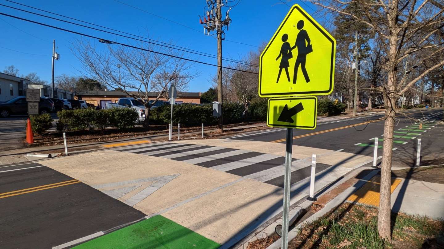 From left to right, a two way road, one lane in each direction with a speed hump and raised pedestrian crossing, bike path, and a pedestrian walking sign.