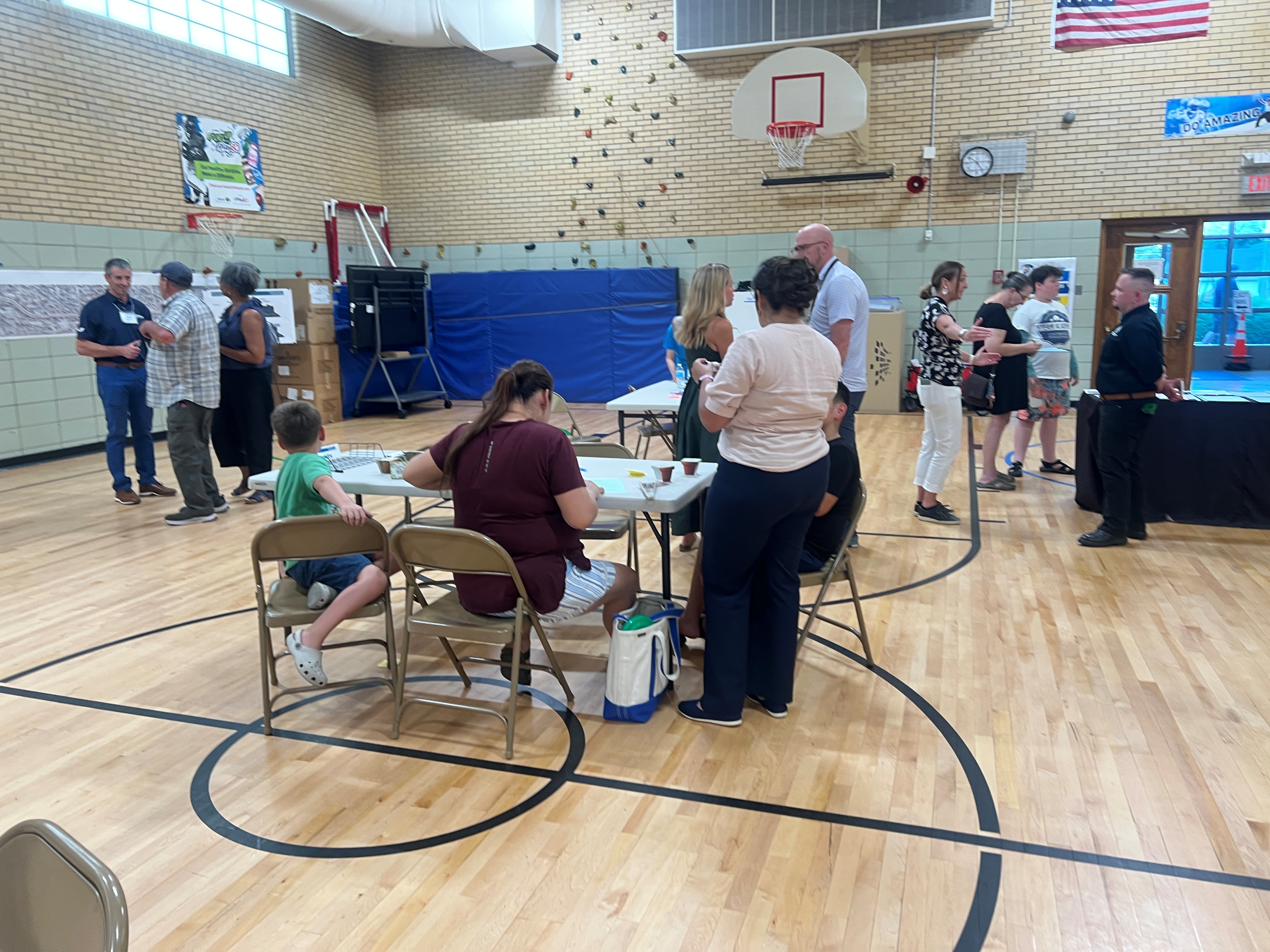 People stand and sit at a table in a school gymnasium