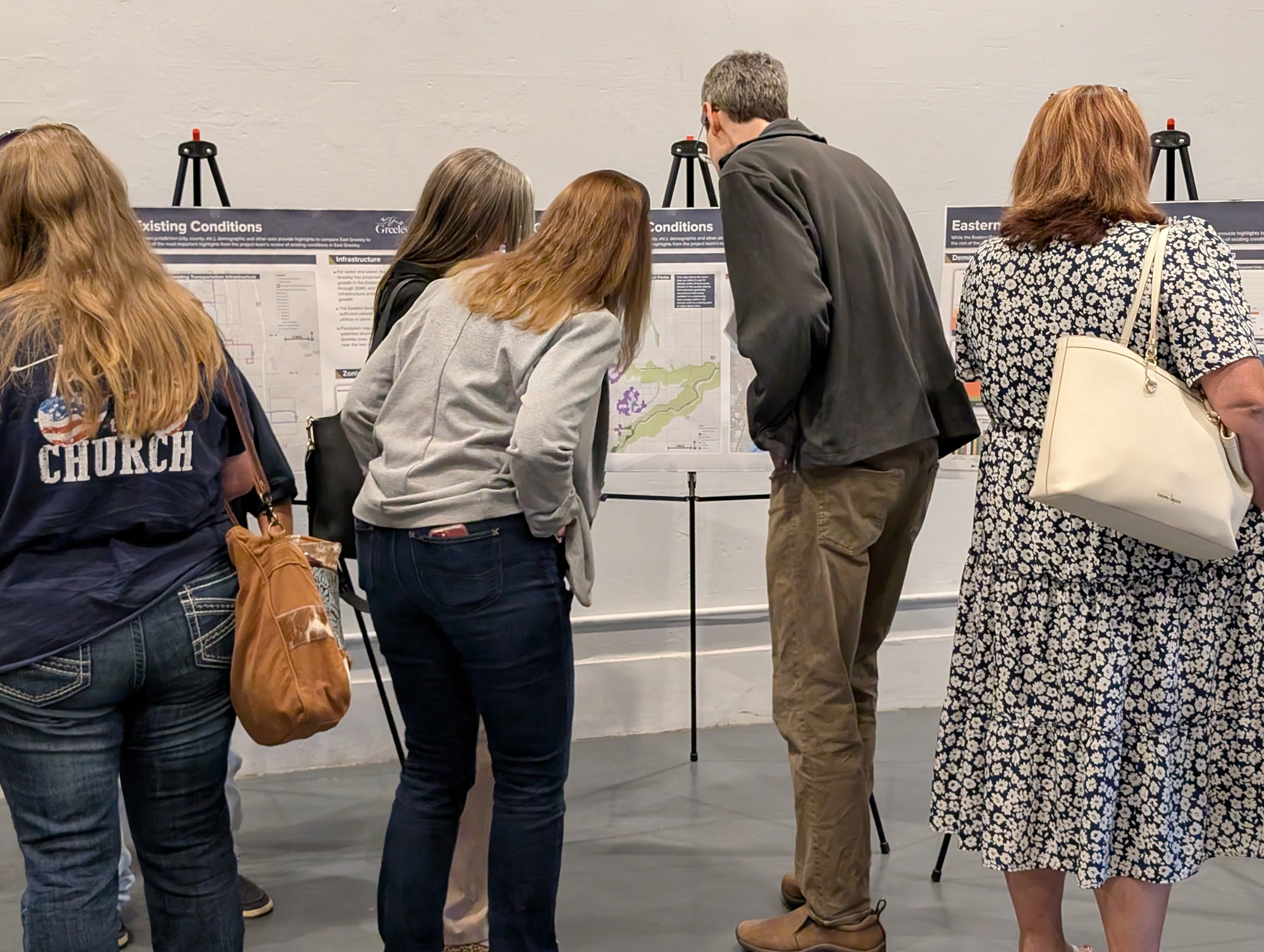 Five people stand near display boards on easels, looking at the information closely.
