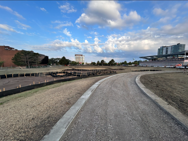 Image shows black fencing and earthwork on the left side, trail with concrete borders in the center, and new Southdale Library in the background on the right side.