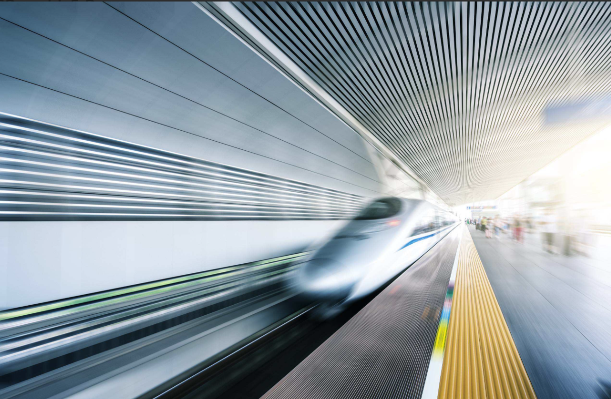 The front of a high-speed train in motion, blurred by its own speed, moving through a metallic tunnel.