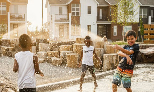 Several children play together in a water feature with homes in the background