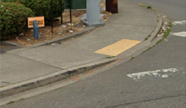  Image showing a part of a crosswalk, marked with white paint, leading to a non-compliant curb ramp. 