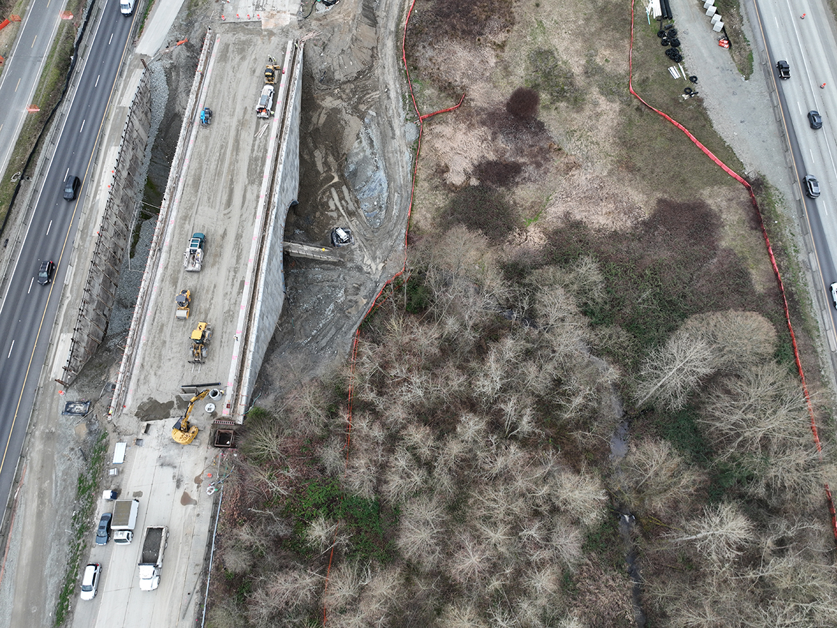 I‑5 Secret Creek southbound overpass under construction with workers finishing the new bridge deck above the creek and trees.