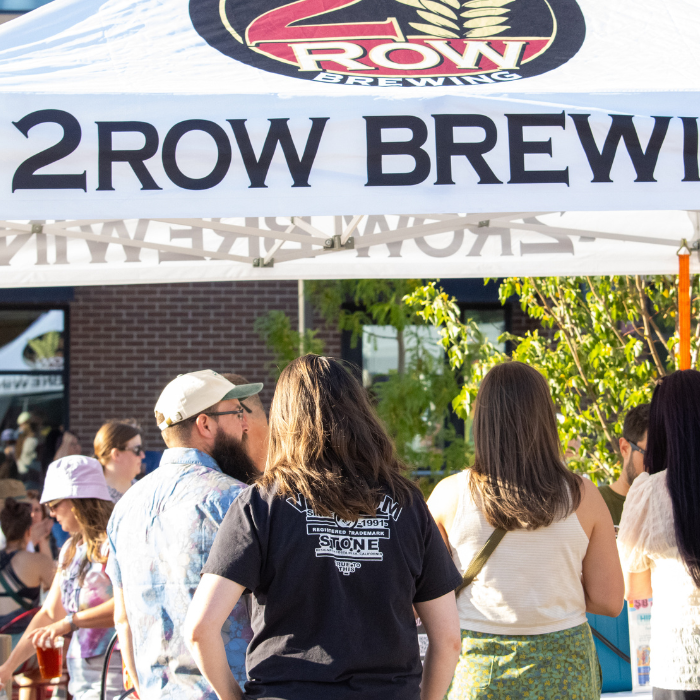 A crowd of people gathered under a tent for "2ROW BREWING," with various individuals visible from behind.