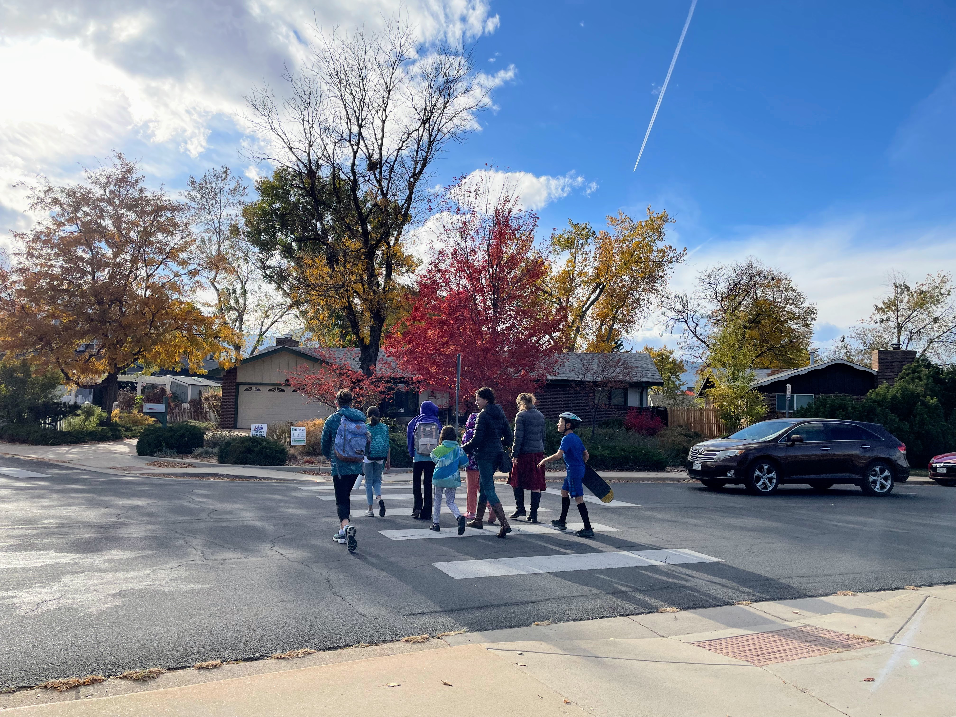 A group of 5 children and 2 adults cross Manhattan Drive at the Iroquois Drive intersection and a driver yields to them.