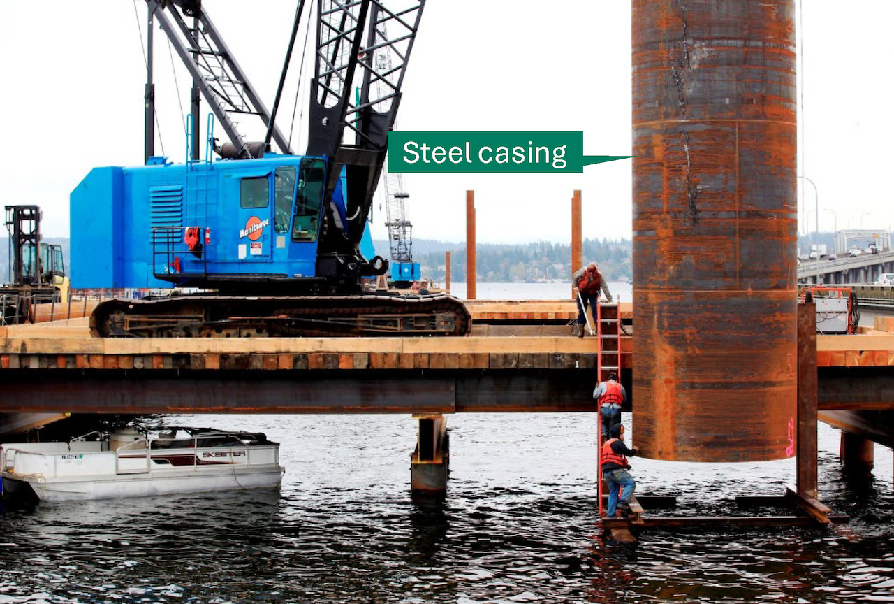 A closer view of a steel casing lowered into water by a crane