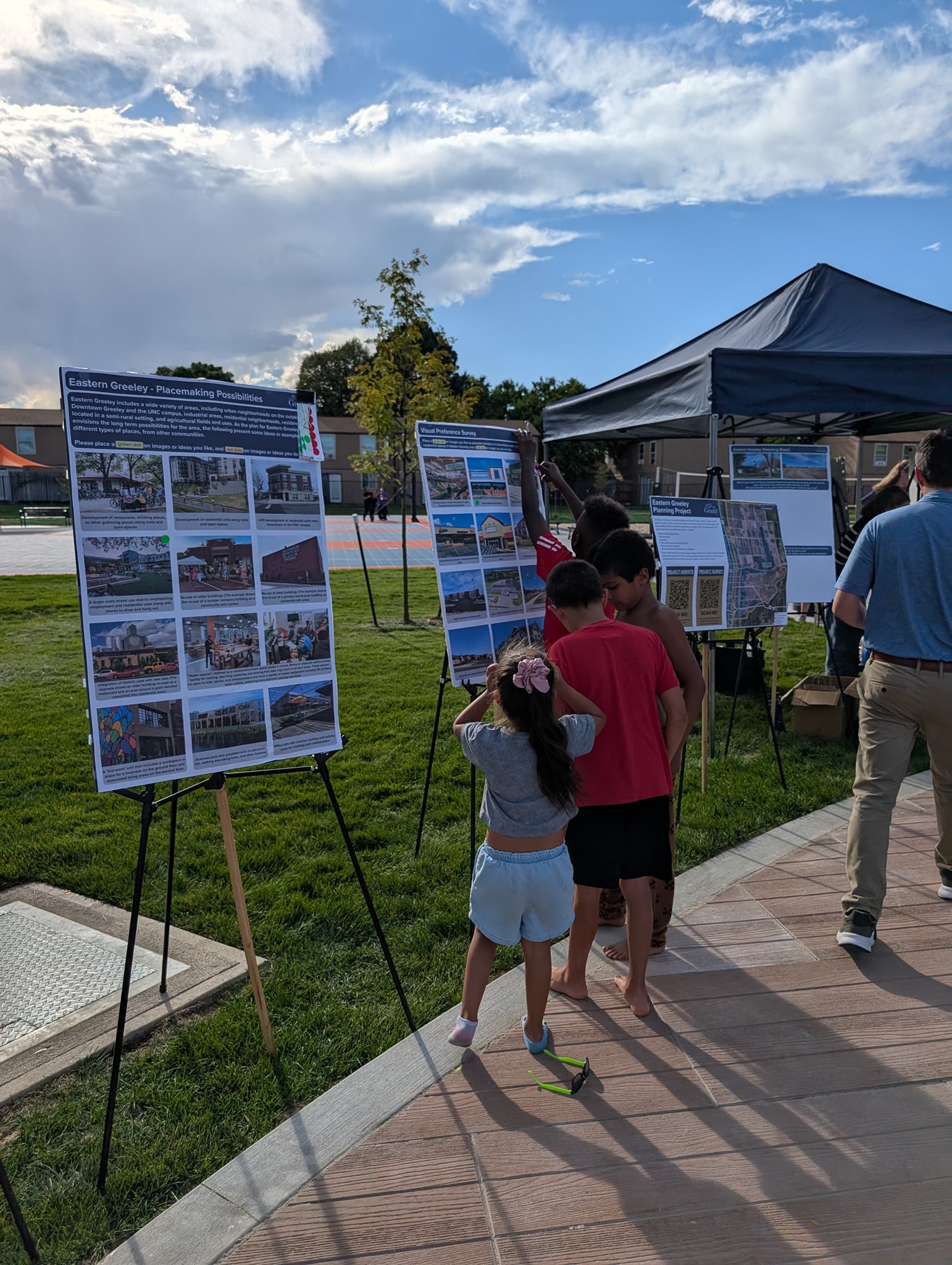People stand in front of boards on easels, They are placing dots on their preferred images.