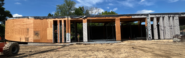 Wide shot of the exterior of Westonka Library construction site. The left side of the building has wood walls going up and the right side of the building has several openings allowing light into the interior space.