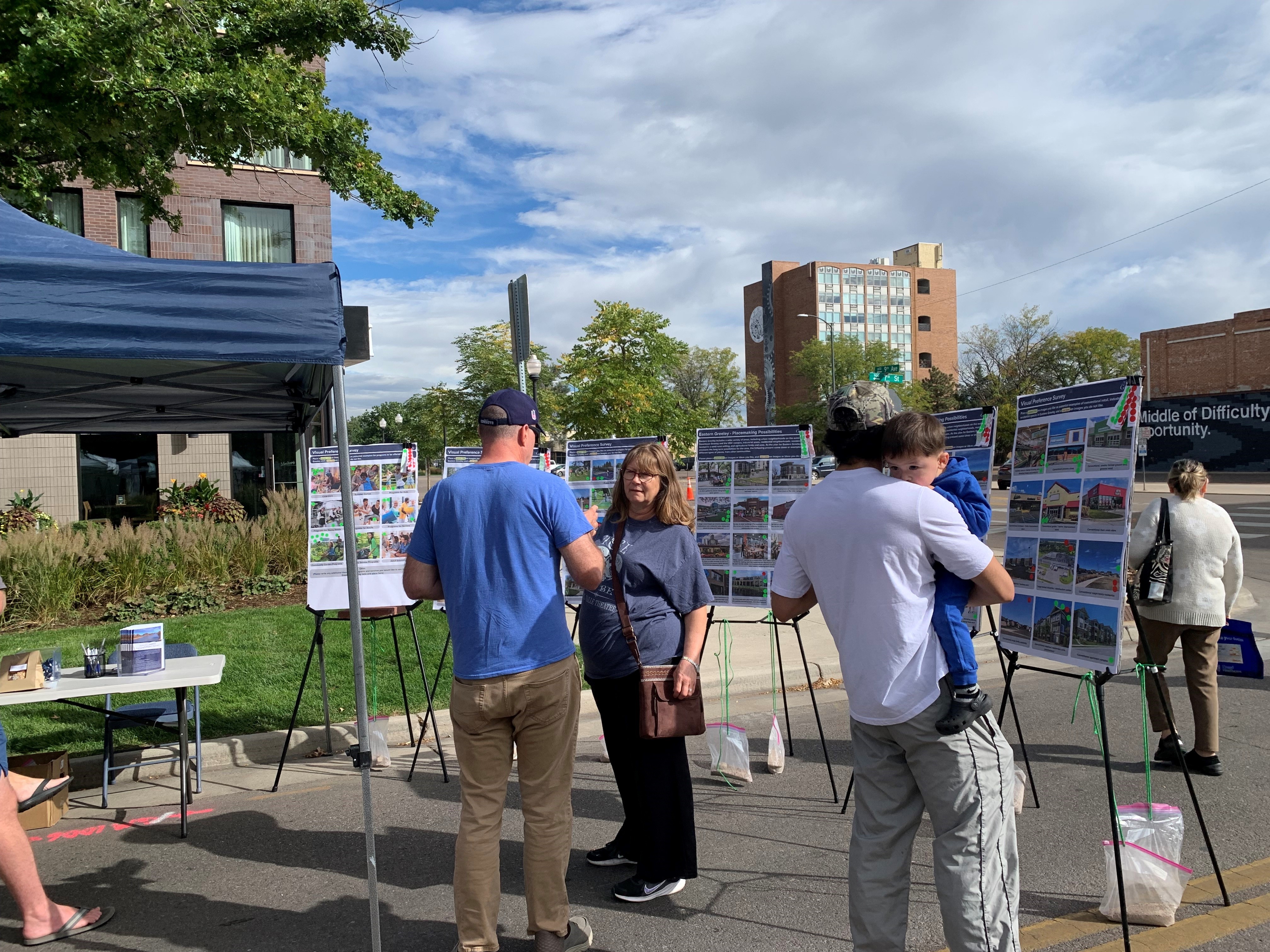 A group of people stand outside in front of display boards at a Farmers' Market.