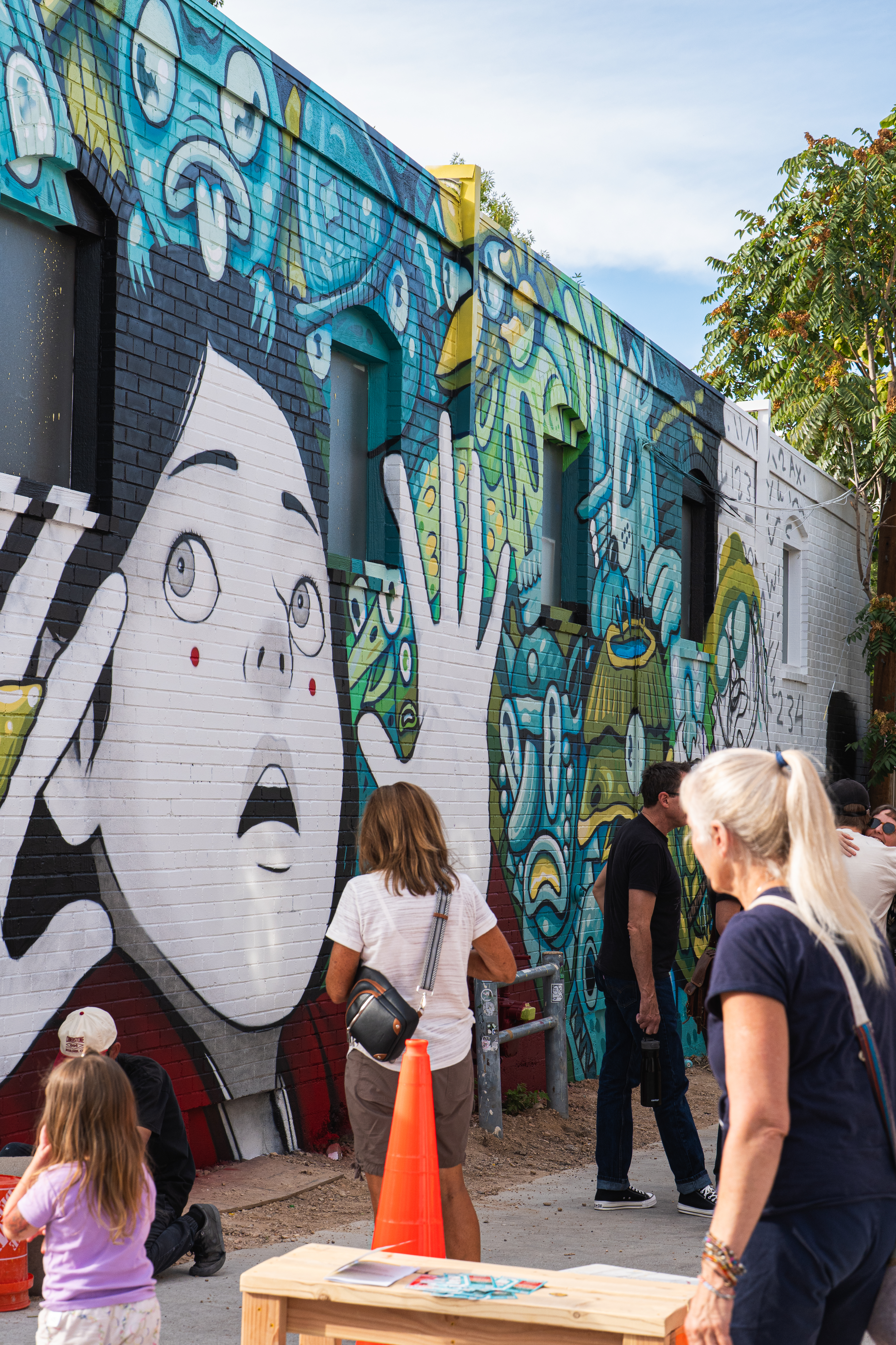 Spectators view a colorful mural in progress during the WeldWalls Mural Festival near 16th Street.