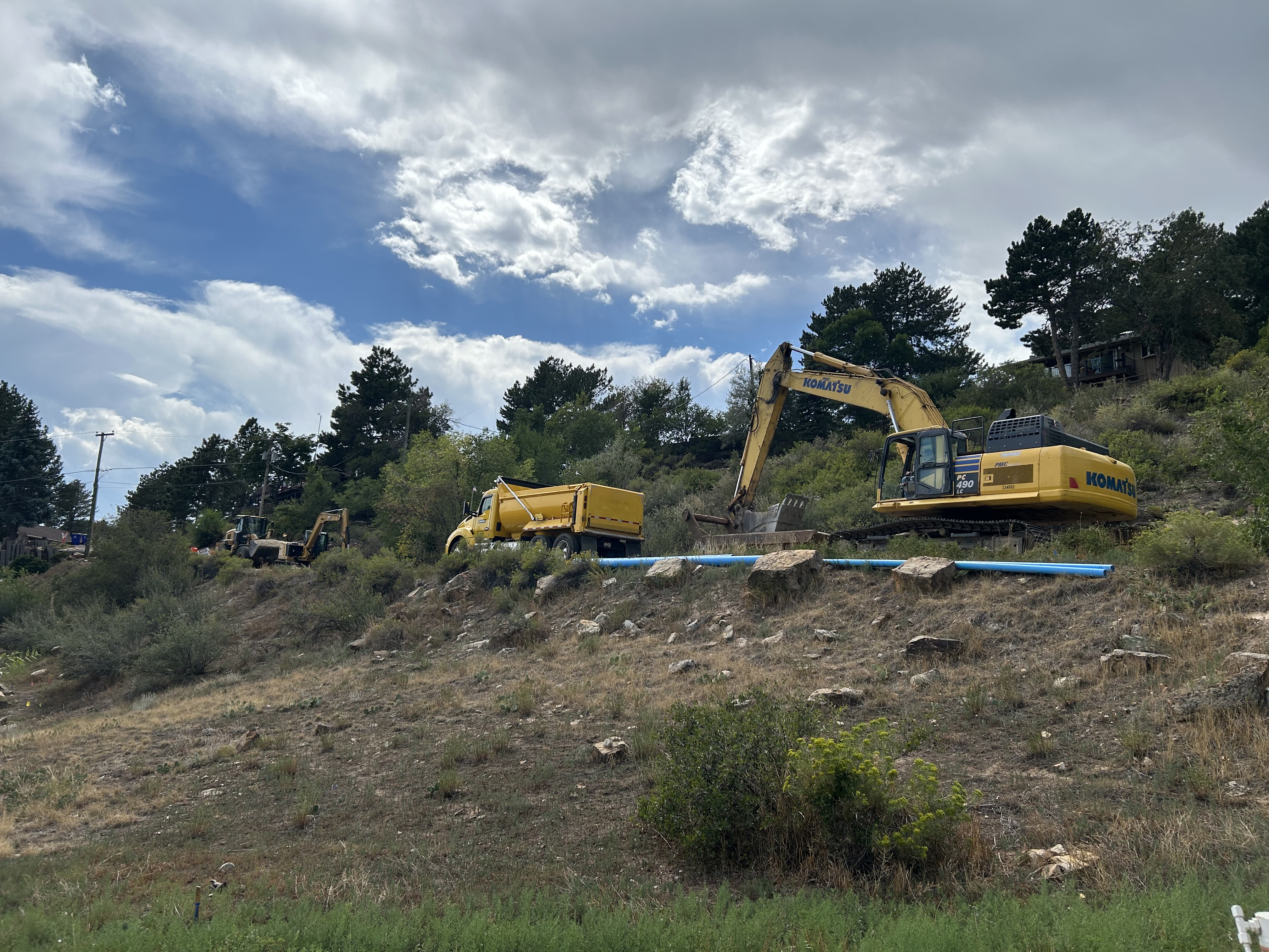 View looking up at construction equipment on the roadside going up a hill with blue sky background.