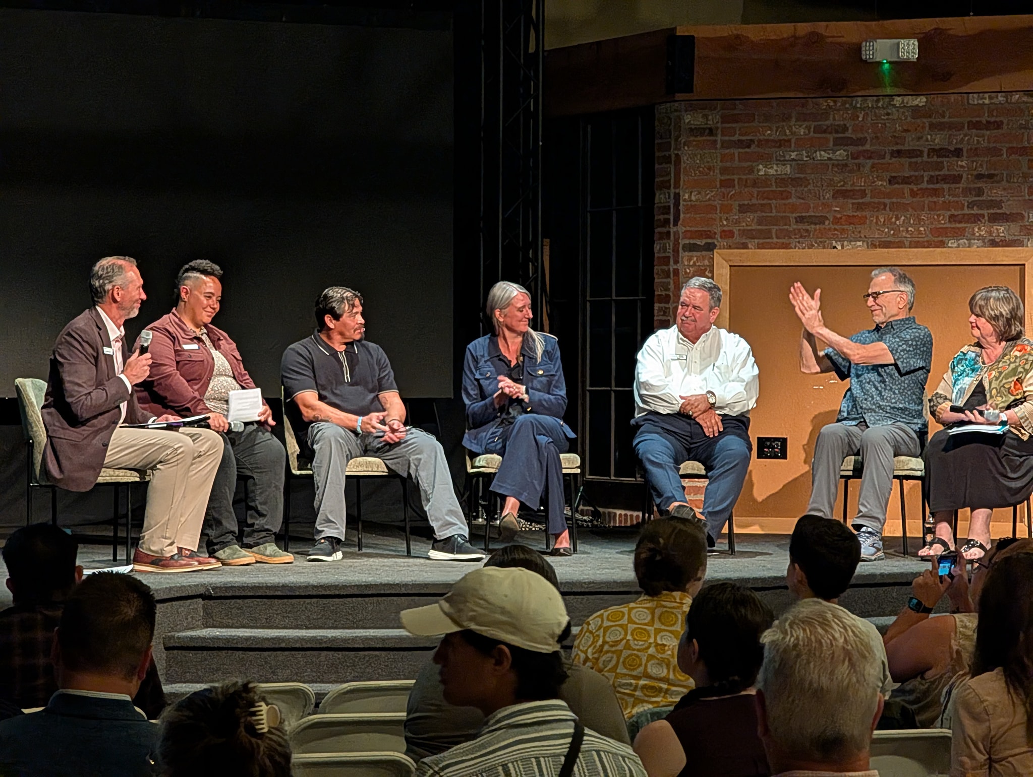 A panel of seven people sit on stage discussing their impressions of the documentary.