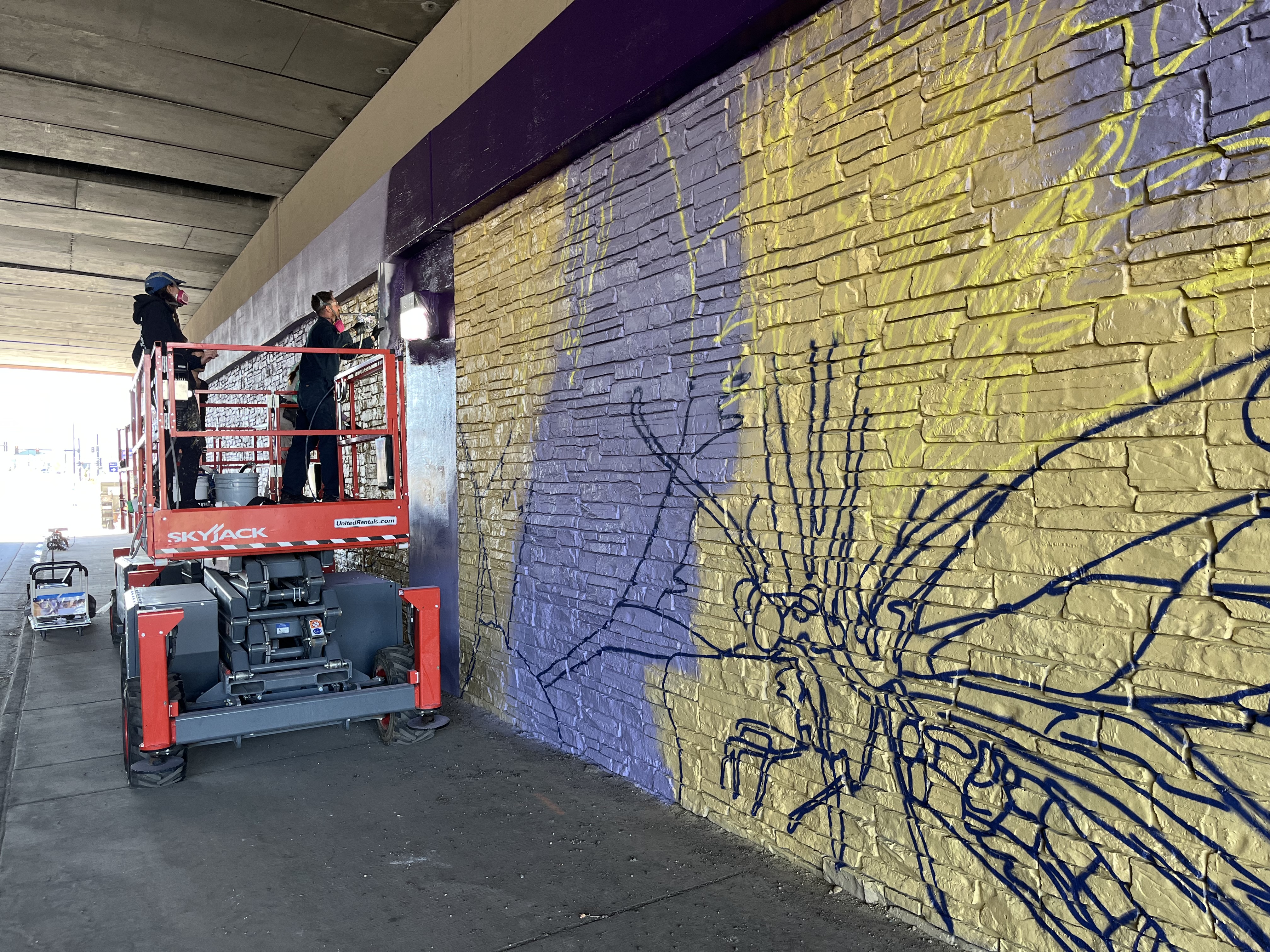 Artist on scaffolding painting mural on underside of bridge