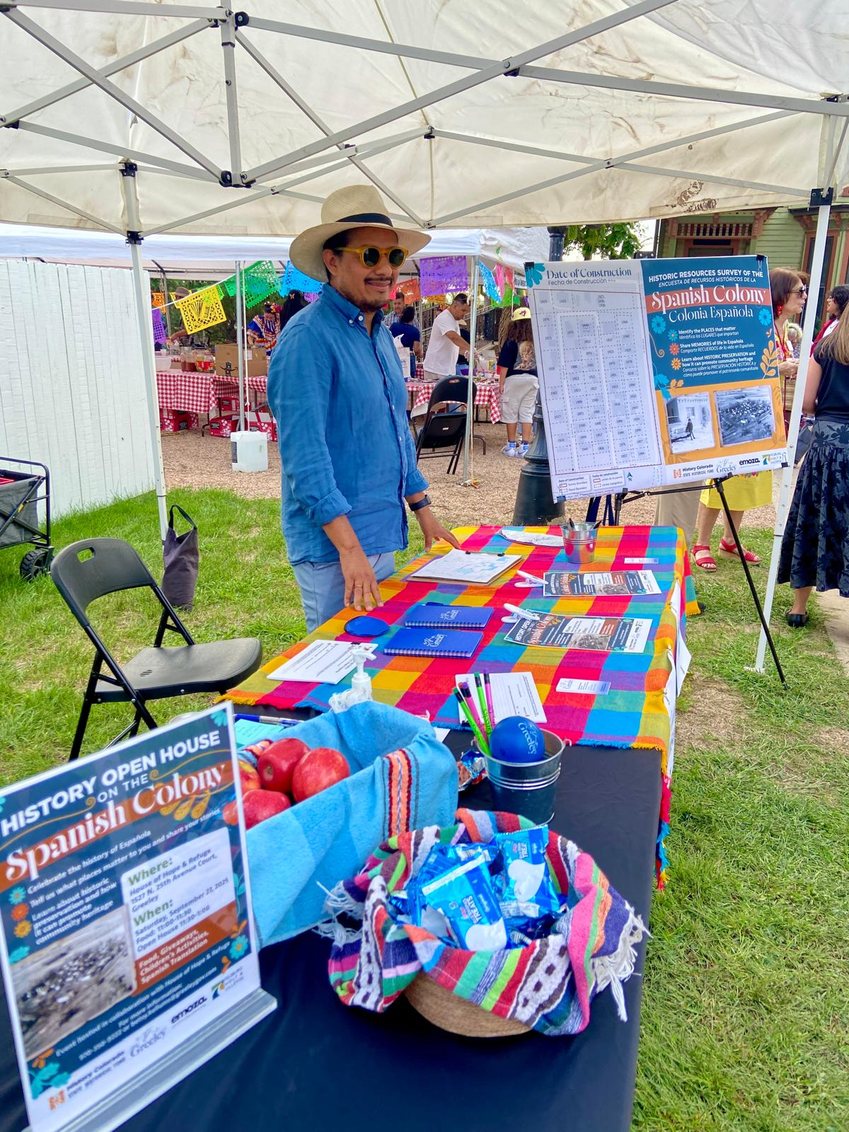 A man stands behind a table at the Fiesta in the Plaza. The table is covered with giveaways and open house event event.