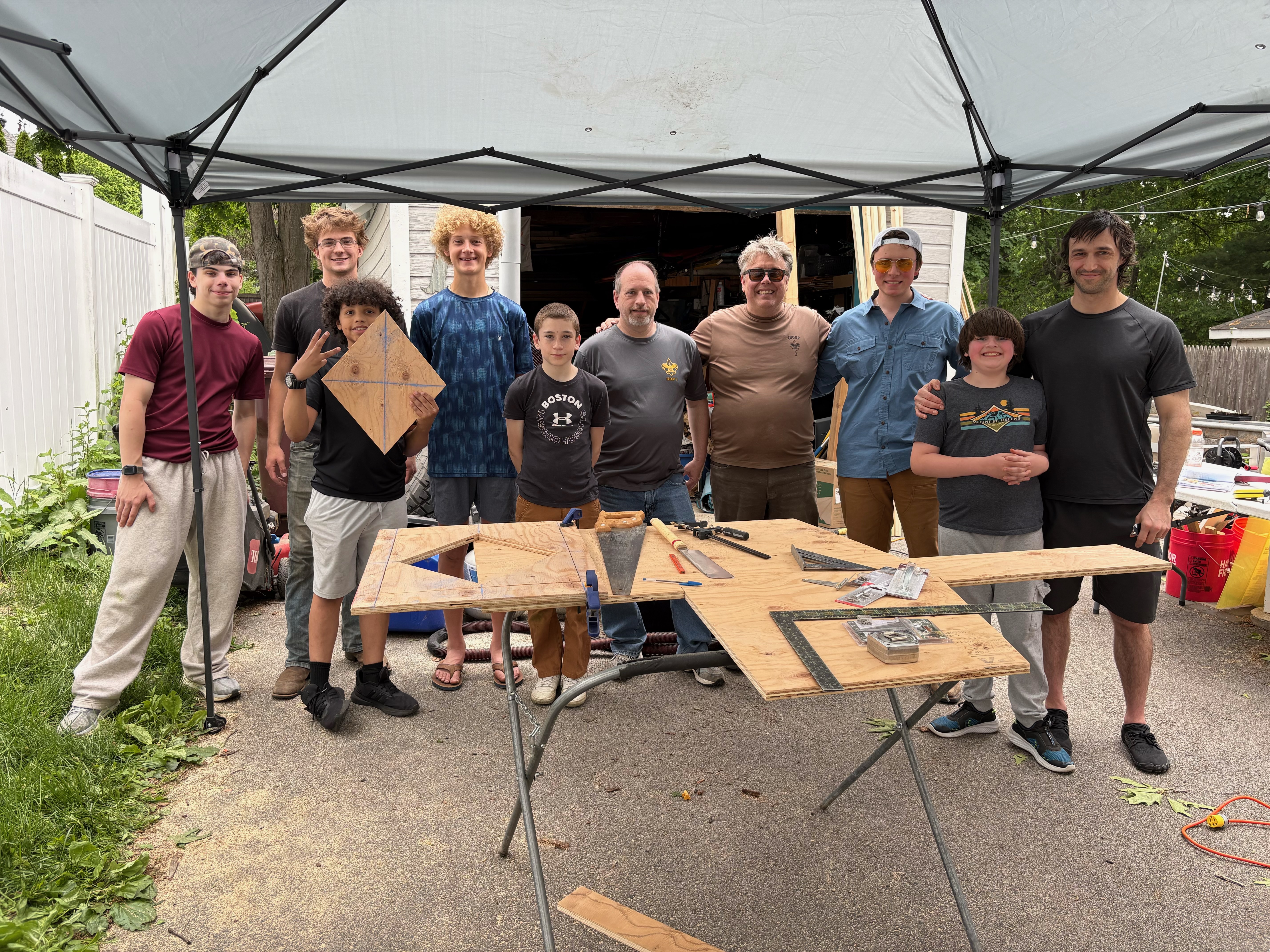 A group of children and adults from an Eagle Scout troop pose under a tent with construction materials to build a native seed library. 