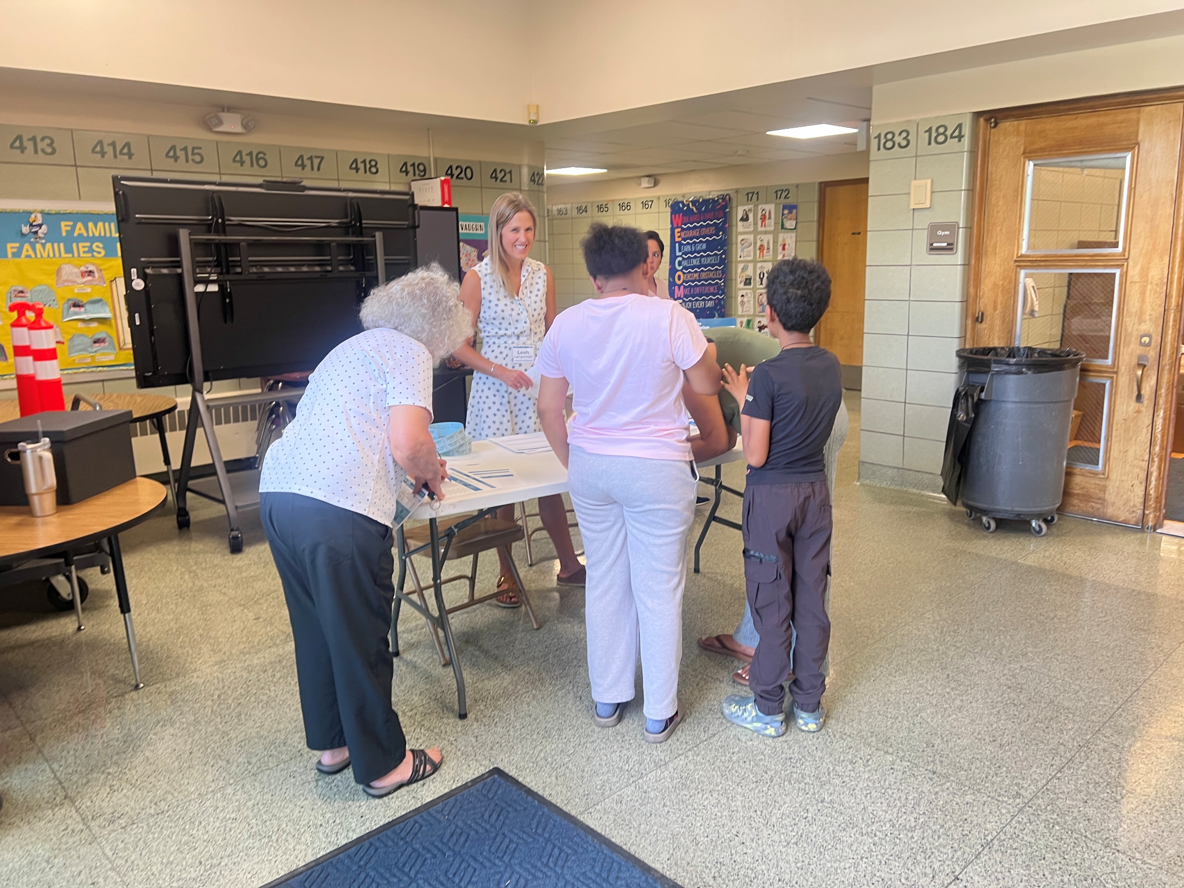 Three people stand at a table talking with a woman