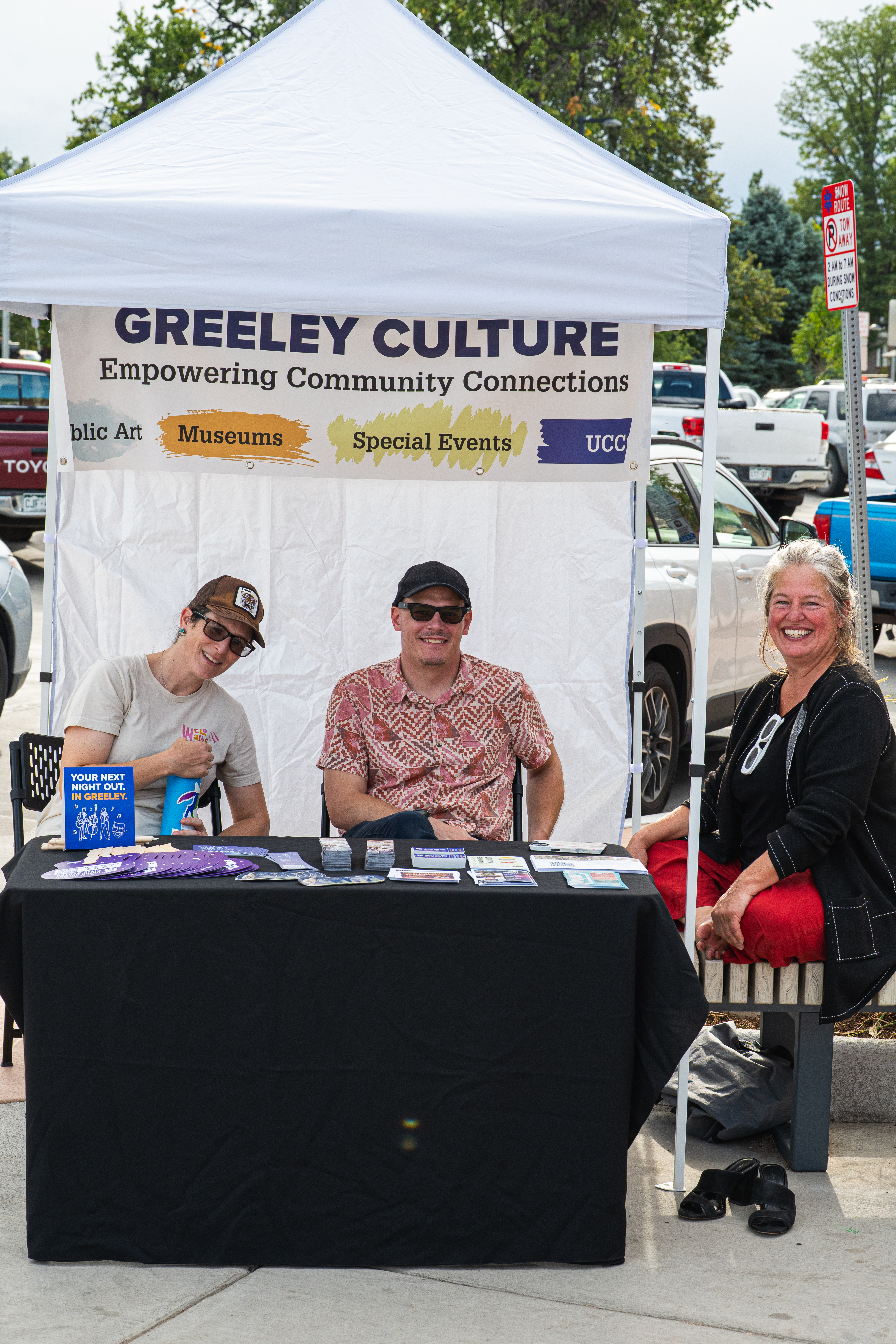 Three people smile at the Greeley Culture booth during the 16th Street celebration and Bear Bash.