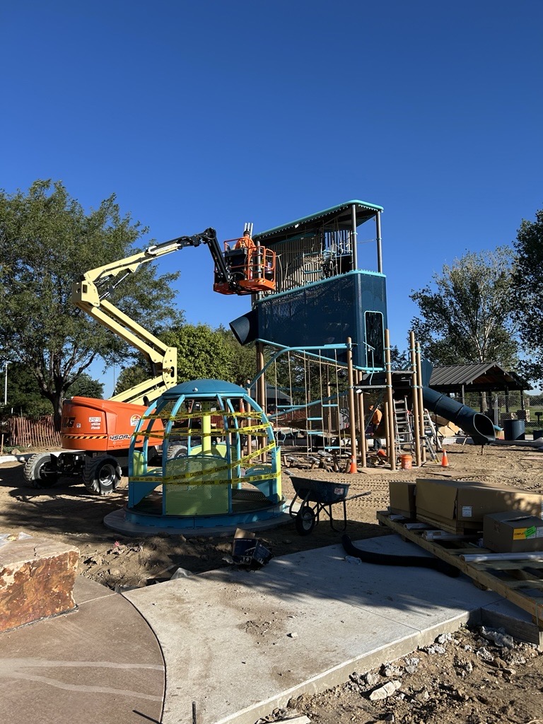 A crane erects a tall piece of playground equipment.
