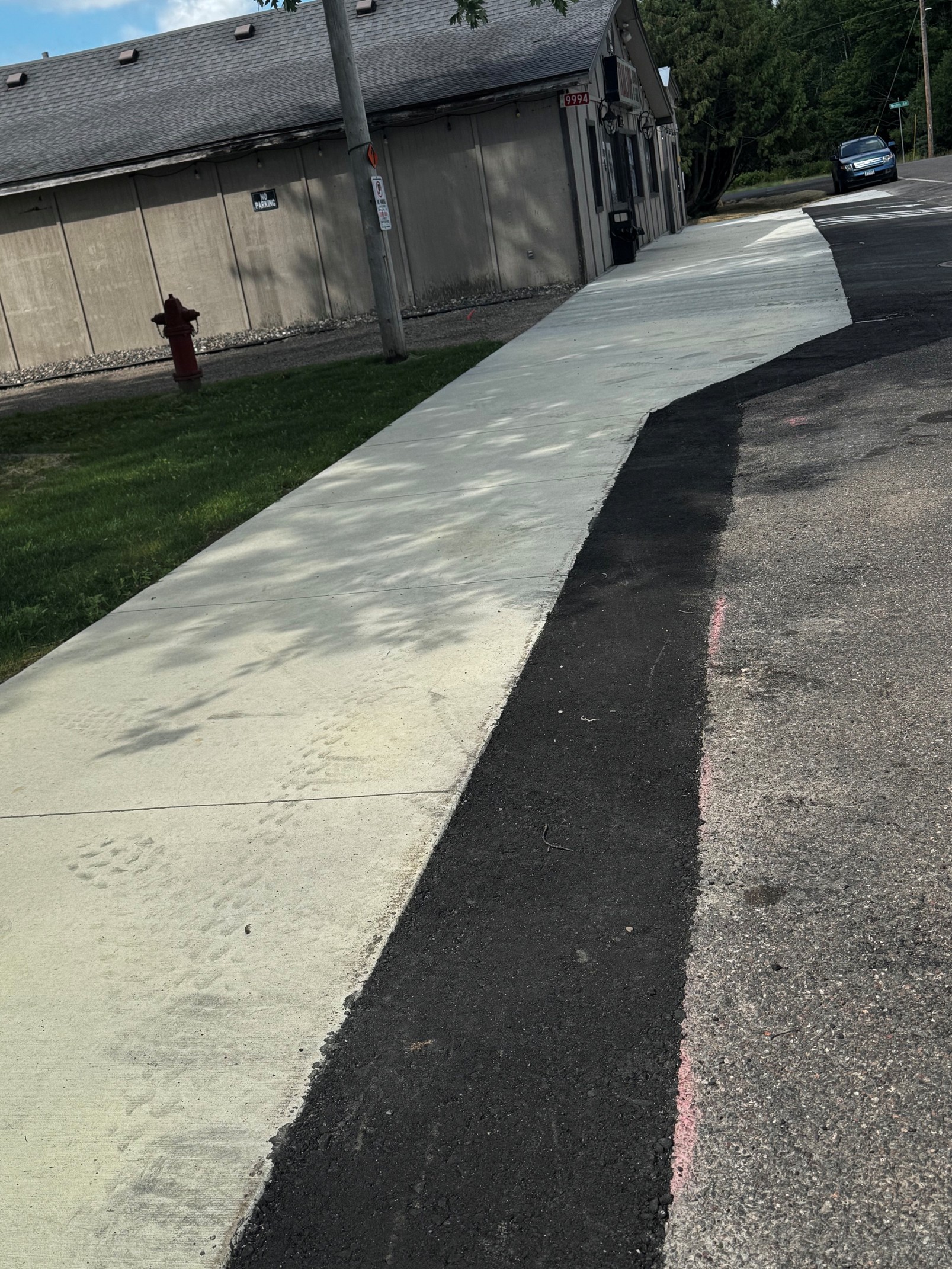 Sidewalk transitions from grey concrete to dark asphalt, with a red fire hydrant and a multifaceted building in the background.