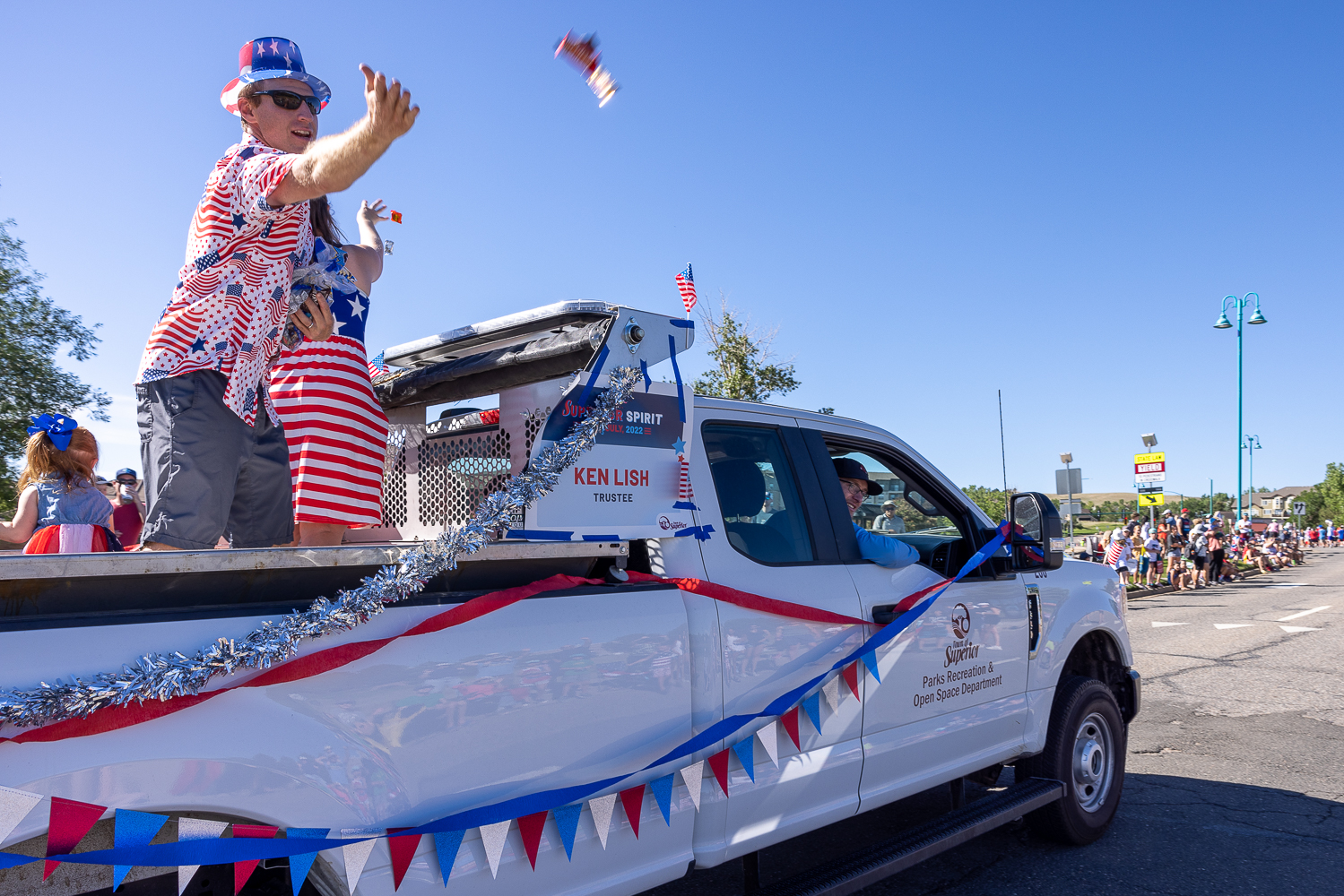 Man in red, white and blue tossing candy from a streamer-decorated truck during a parade