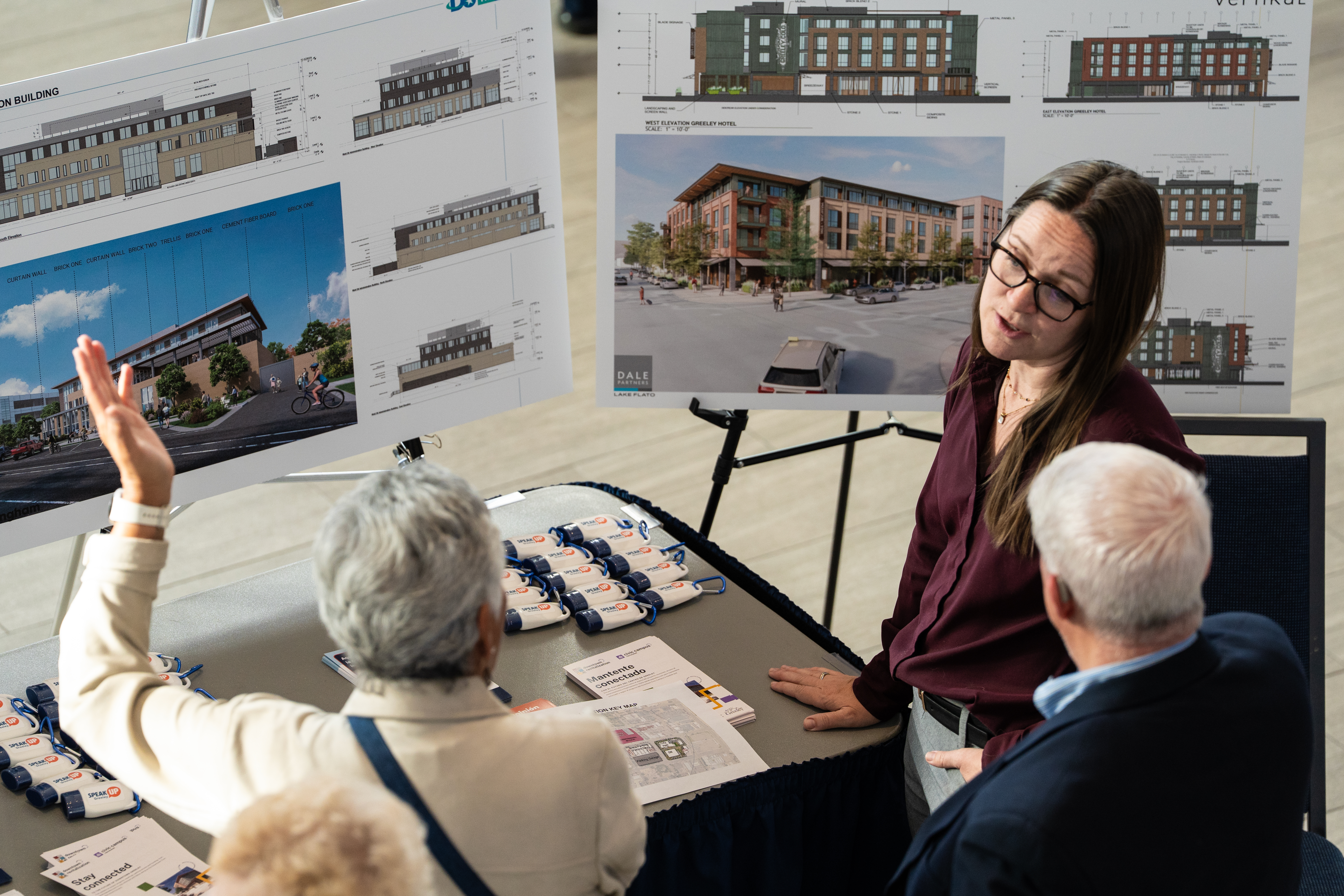 Project representative chats with two community members with renderings behind her.
