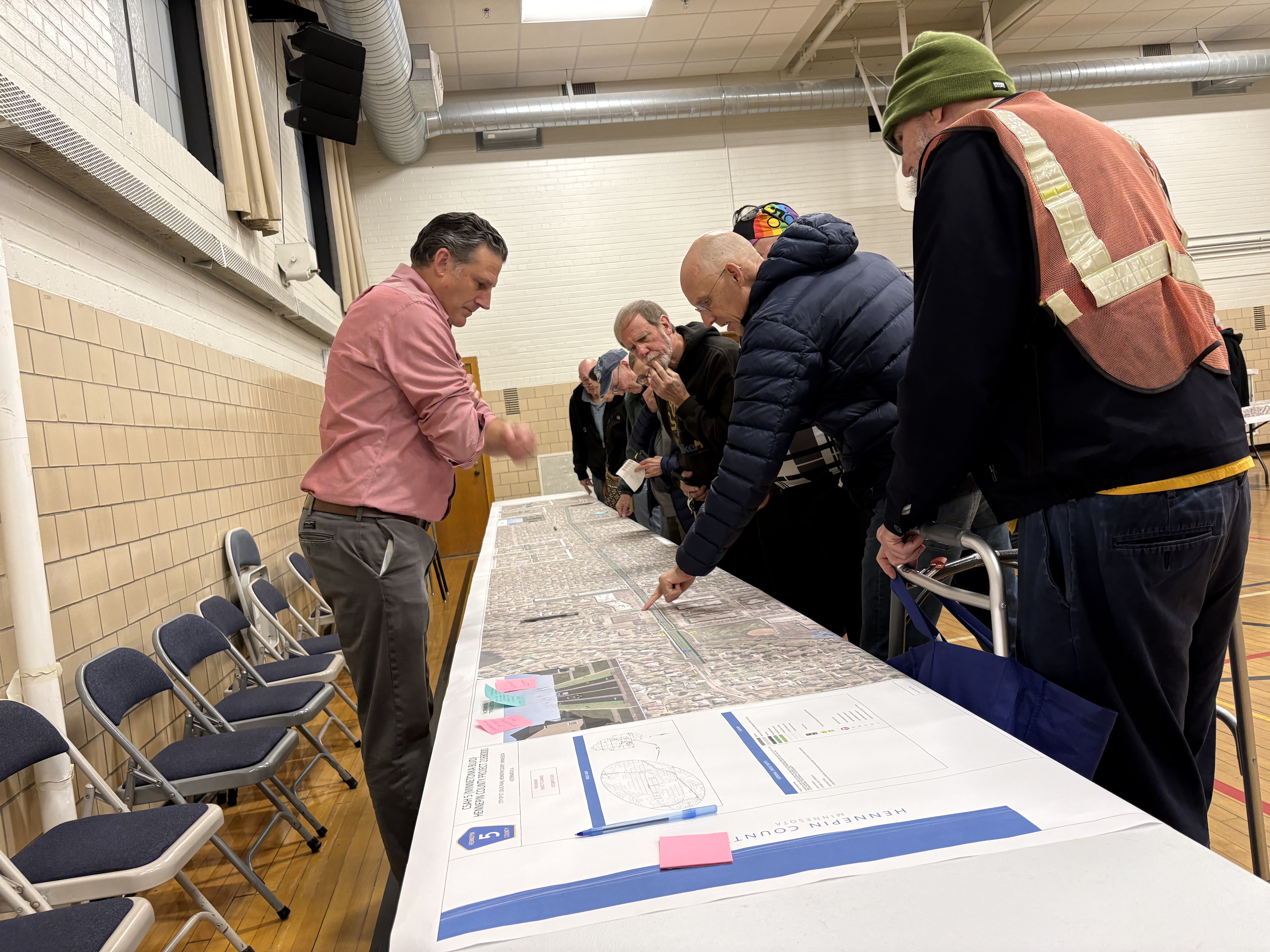 A man is pointing at a map on a table of Minnetonka Boulevard. Other people are looking at the map.