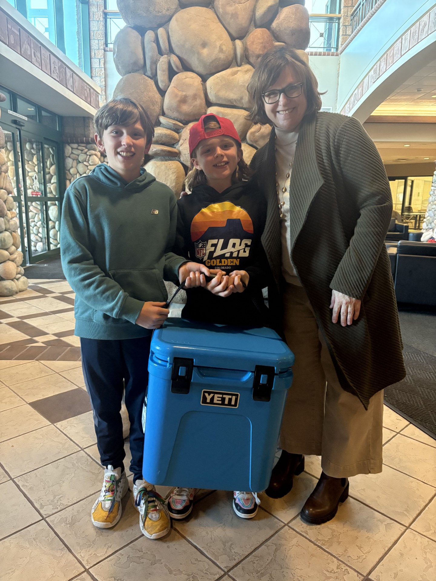 Woman and two boys smiling with blue yeti cooler in the Recreation Center lobby
