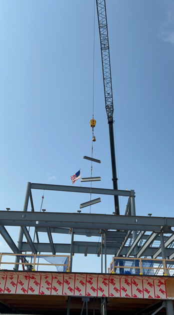 Large crane lifts three horizontal beams into the air resembling a wind "chime" and prepares to set them in place at Southdale Library