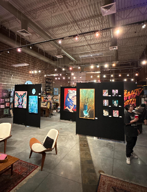 Midvale Main Art House gallery with colorful artwork on black panels, warm string lights, and a visitor walking through.