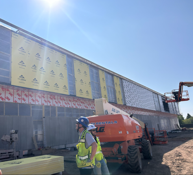 Exterior walls of Southdale Library going up with two crew members in the foreground, large lift behind them, and building under construction in the background.