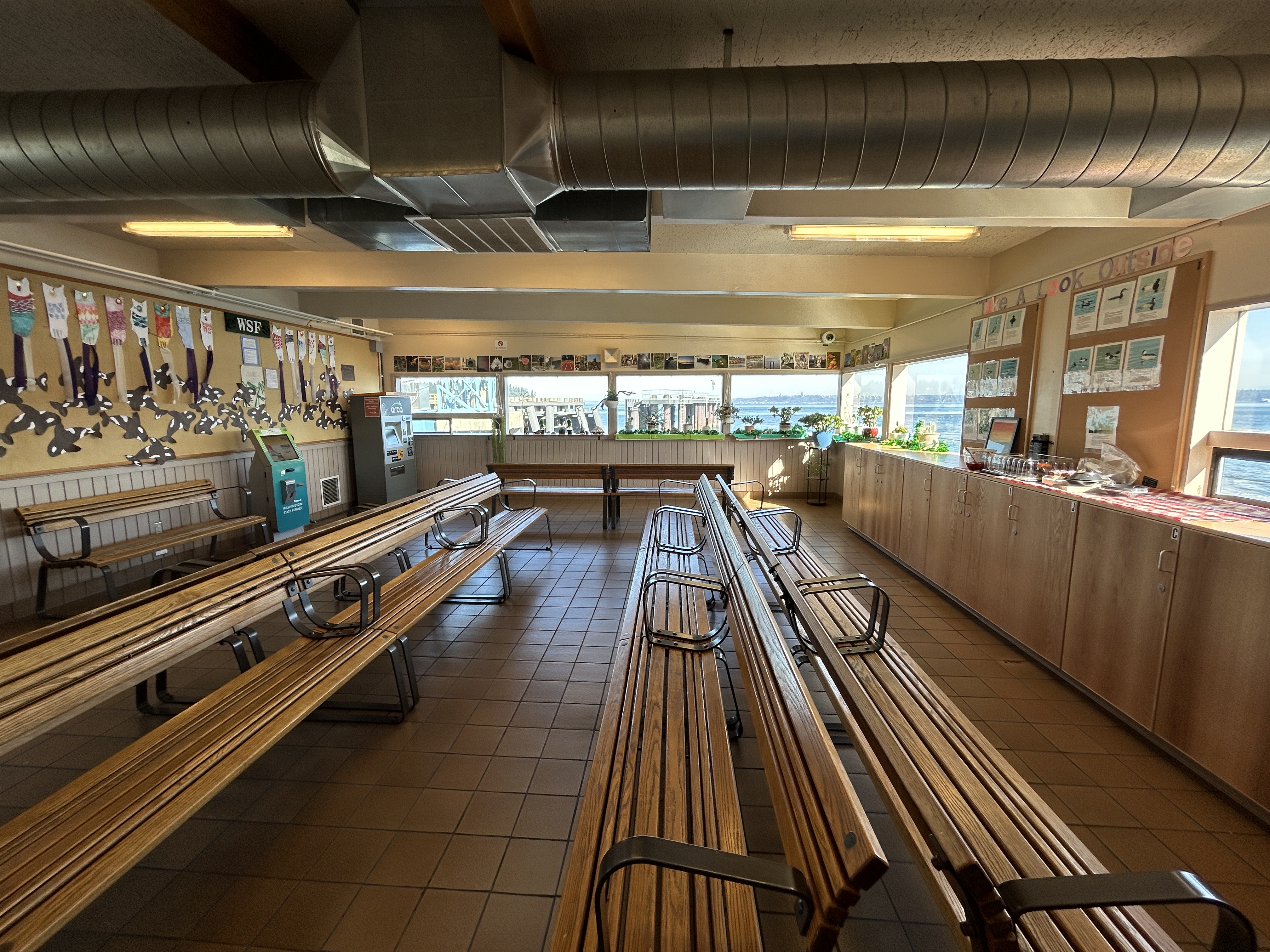 The inside of the terminal building with long benches for seating, orca artwork on the walls and windows overlooking the water.