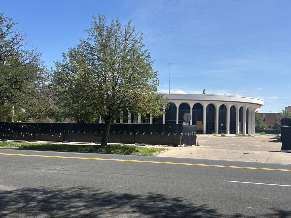 A round building, also known as the former city hall sits behind black demolition fencing