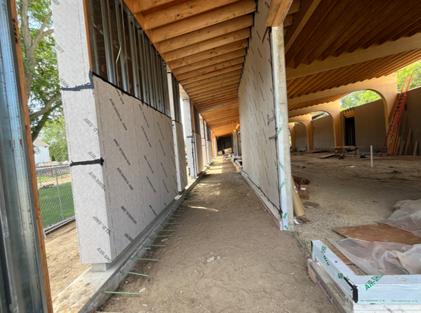 This image shows a covered porch walkway in the center and a large open room with wood beams and ceiling to the right.