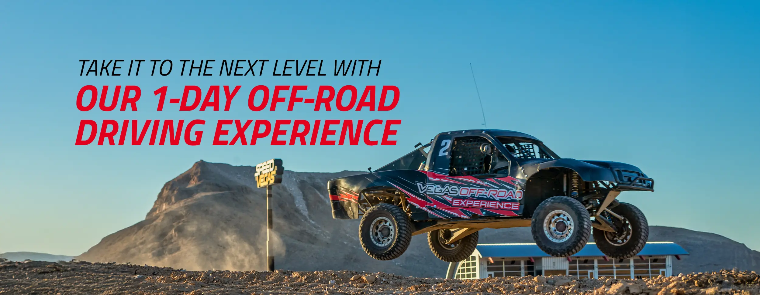 A black off-road race truck with red accents soars over a dirt track against a desert mountain backdrop. Bold text reads "1-Day Off-Road Driving Experience".