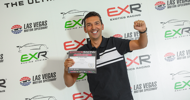 A joyful man in a black polo holds a certificate, raising his fist in celebration. Background features