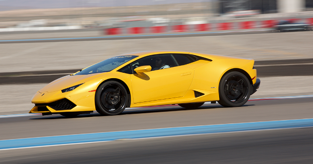 Yellow sports car speeding on a racetrack, creating a dynamic and thrilling atmosphere. The background features blurred red and white barriers.