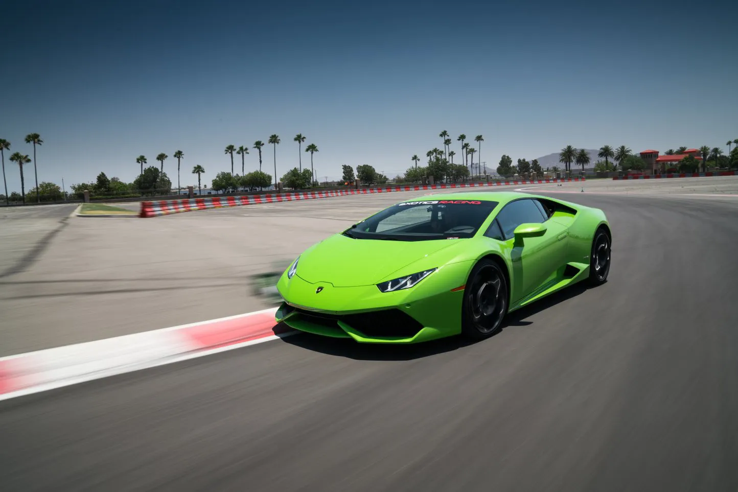 A vibrant green sports car speeds around a racetrack. Palm trees line the track under a clear blue sky, conveying excitement and motion.